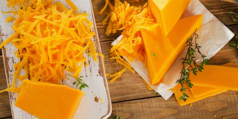 cheddar cheese, solid block and grated on wooden cutting board and parchment paper. 