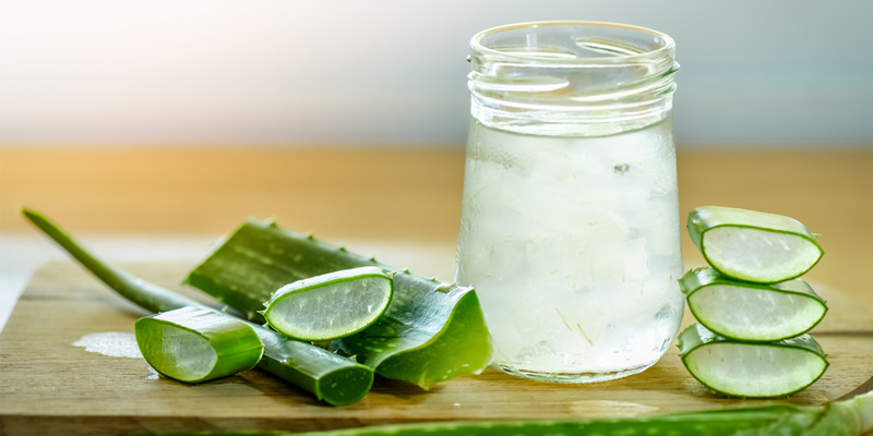 jar of collected aloe vera gel with slices on wooden board.